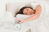 cute woman waking under sheet turning off alarm clock