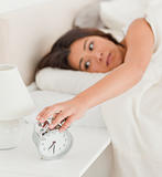 charming woman waking under sheet turning off alarm clock