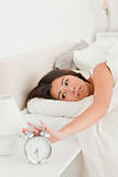 gorgeous woman waking under sheet turning off alarm clock