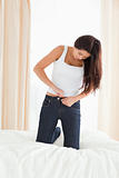 pretty woman kneeing on bed trying to close her jeans