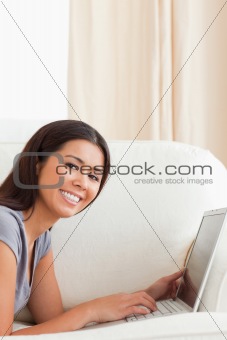 close up of a smiling woman lying on sofa with notebook looking 