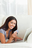 charming woman with card in hand lying on sofa looking into came