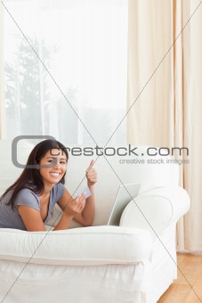 woman with thumb up and card in hand lying on sofa looking into 