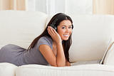 smiling woman with earphones lying on sofa looking into camera