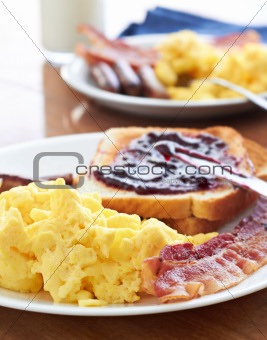 breakfast with scrambled eggs and bacon with toast with jam.