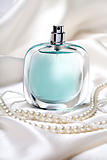 Blue perfume bottle and pearl necklace on the white silk background