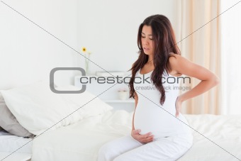 Beautiful pregnant woman holding her back while sitting on a bed