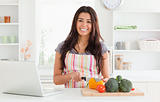 Beautiful woman relaxing with her laptop while cooking vegetables