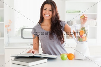 Beautiful woman consulting a notebook while filling a blender 