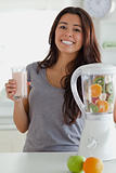 Lovely woman using a blender while holding a drink