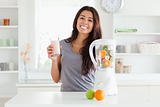 Beautiful woman using a blender while holding a drink