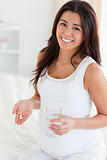 Attractive pregnant woman holding a glass of water and pills
