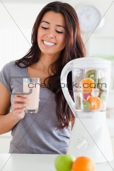 Good looking woman using a blender while holding a drink