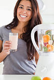 Charming woman using a blender while holding a drink