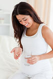 Good looking pregnant woman holding a glass of water and pills 