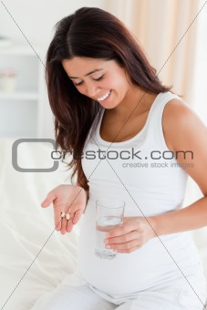 Good looking pregnant woman holding a glass of water and pills 