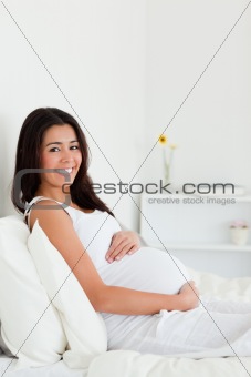 Pretty pregnant woman touching her belly while lying on a bed