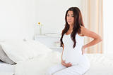 Attractive pregnant woman holding her back while sitting 