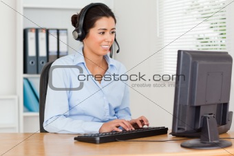 Attractive woman with a headset helping customers while typing 