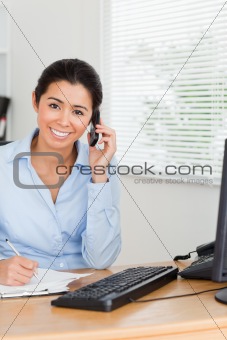 Attractive woman using her mobile phone while writing 
