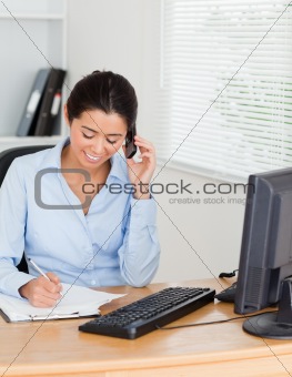 Good looking woman using her mobile phone while writing