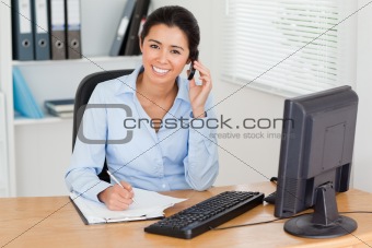 Charming woman using her mobile phone while writing 