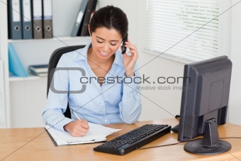 Gorgeous woman using her mobile phone while writing 