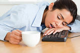 Pretty woman sleeping on a keyboard while holding a cup of coffee