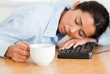 Beautiful woman sleeping on a keyboard while holding a cup