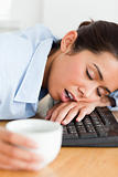 Good looking woman sleeping on a keyboard while holding a cup