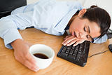 Attractive woman sleeping on a keyboard while holding a cup 
