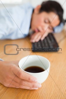 Cute woman sleeping on a keyboard while holding a cup of coffee