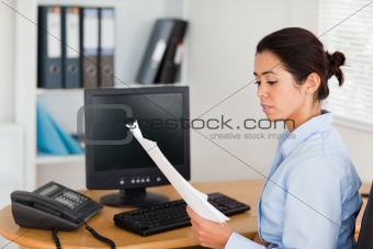 Pretty woman holding and looking at a sheet of paper while sitting