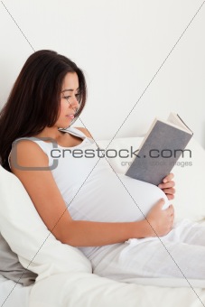 Charming pregnant woman reading a book while lying on a bed