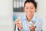 Charming woman holding keys and a miniature house while looking 