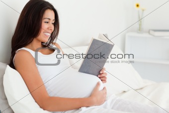 Good looking pregnant woman reading a book while lying on a bed