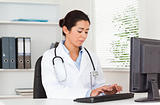 Charming female doctor typing on a keyboard while sitting