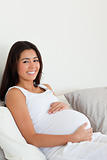 Lovely pregnant woman touching her belly while lying on a bed
