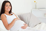 Cute pregnant woman touching her belly while lying on a bed