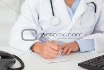Female doctor with a stethoscope writing on a scratchpad
