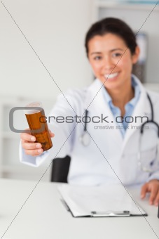 Pretty smiling doctor holding a box of pills while sitting