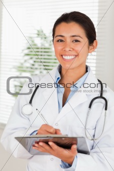 Attractive female doctor with a stethoscope writing on a notebook