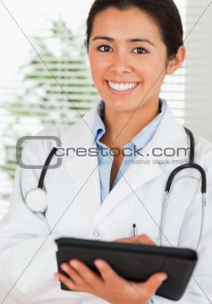 Good looking female doctor with a stethoscope writing on a notebook