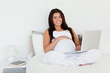 Pretty pregnant woman relaxing with her laptop while