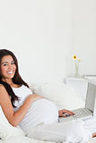 Cute pregnant woman relaxing with her laptop while