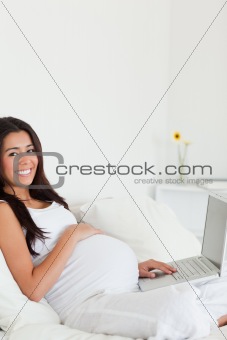 Cute pregnant woman relaxing with her laptop while