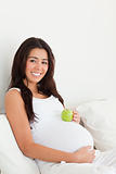 Gorgeous pregnant woman holding an apple on her belly 