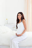 Attractive pregnant woman touching her belly while sitting