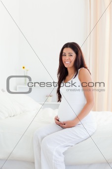 Attractive pregnant woman touching her belly while sitting