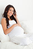 Good looking pregnant woman on the phone while lying on a bed